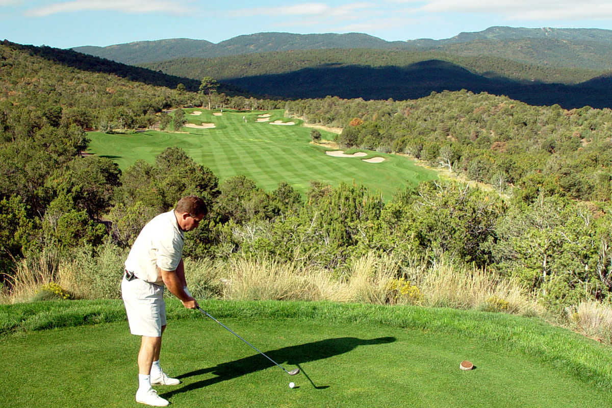 A person playing golf at a scenic course surrounded by lush greenery and rolling hills.