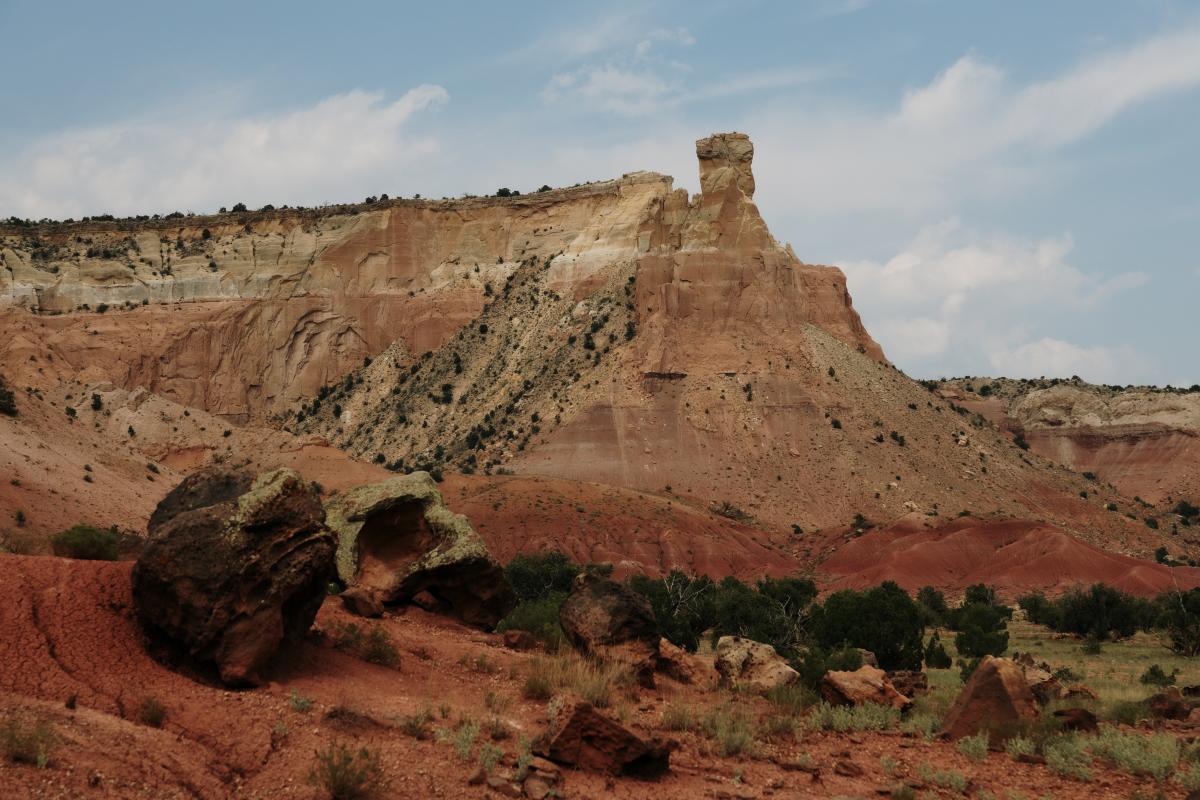 A large cliff with a distinct rock formation on top above shrubbery on a ragged plain.