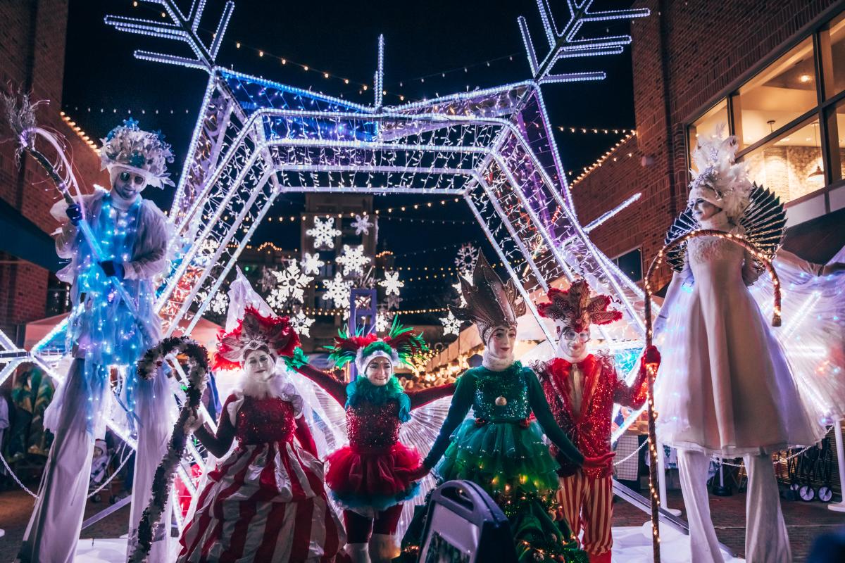 6 entertainers pose in winter costumes at night with Christmas lights