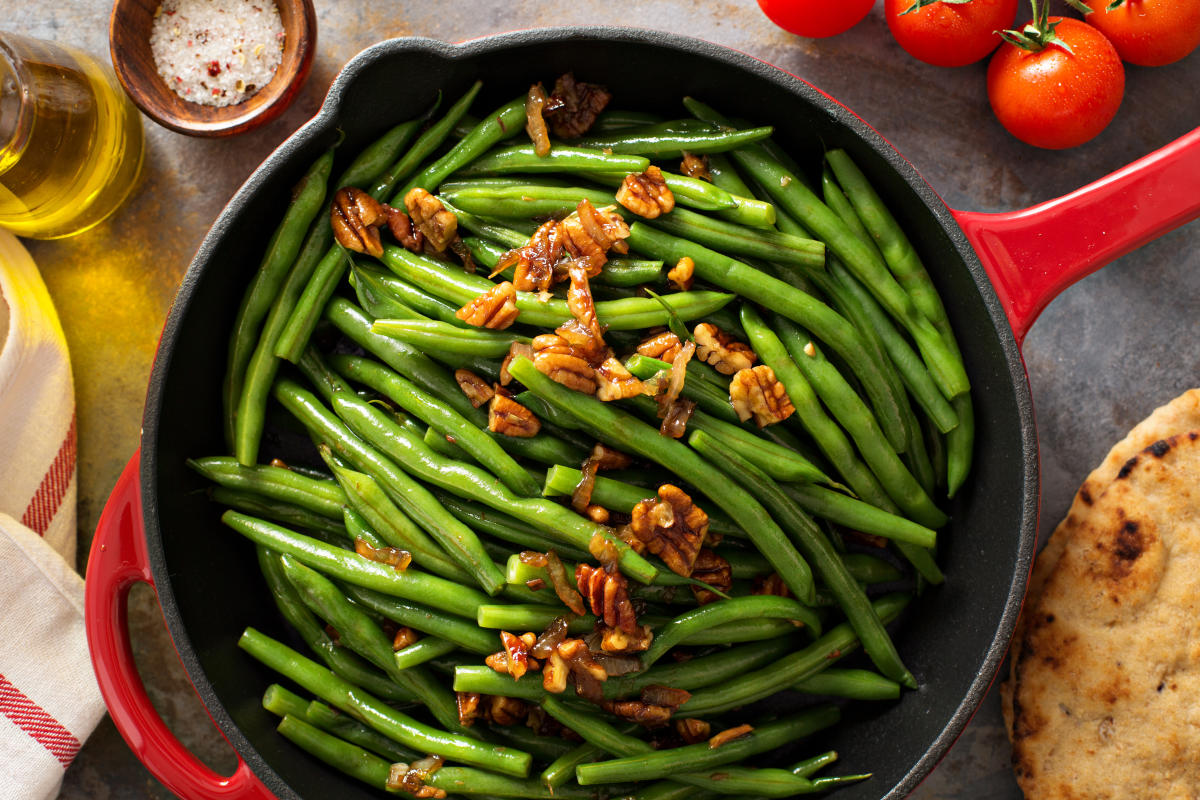 A cast iron skillet contains sautéed green beans topped with pecans.