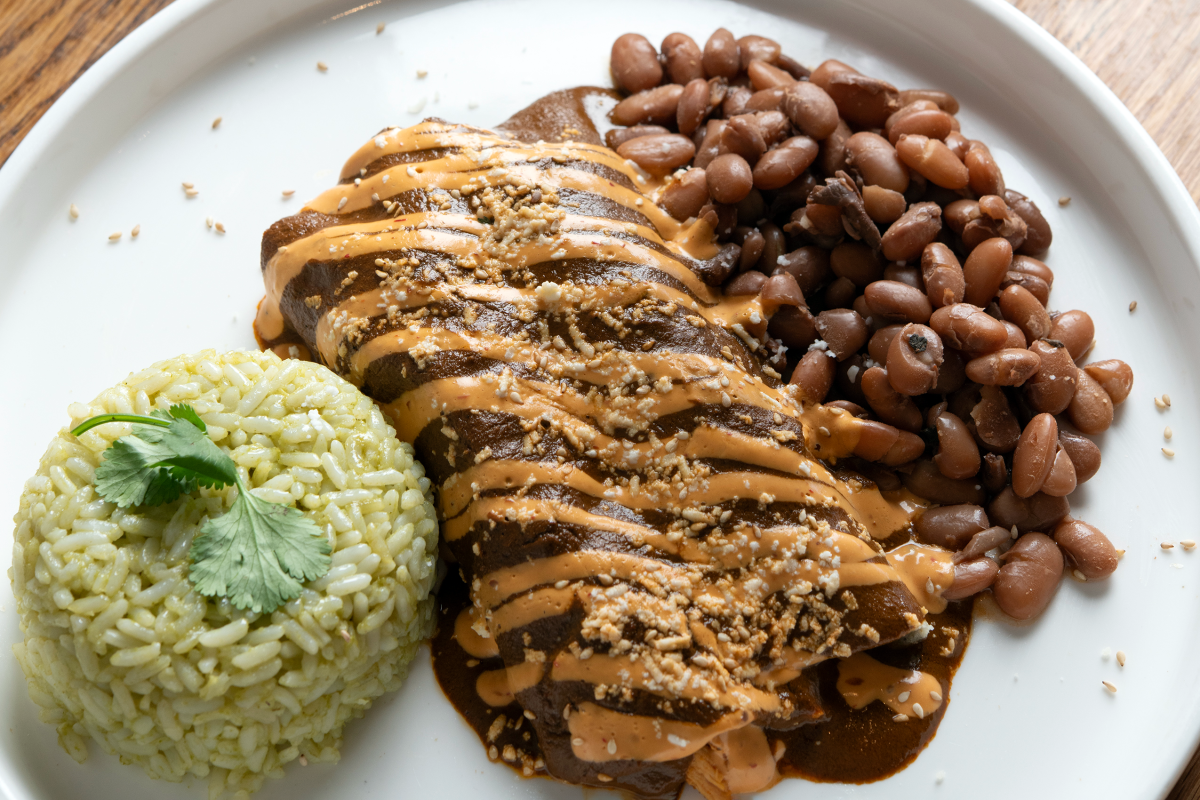 Tender chicken enchiladas topped with mole sauce and a side of beans and rice.