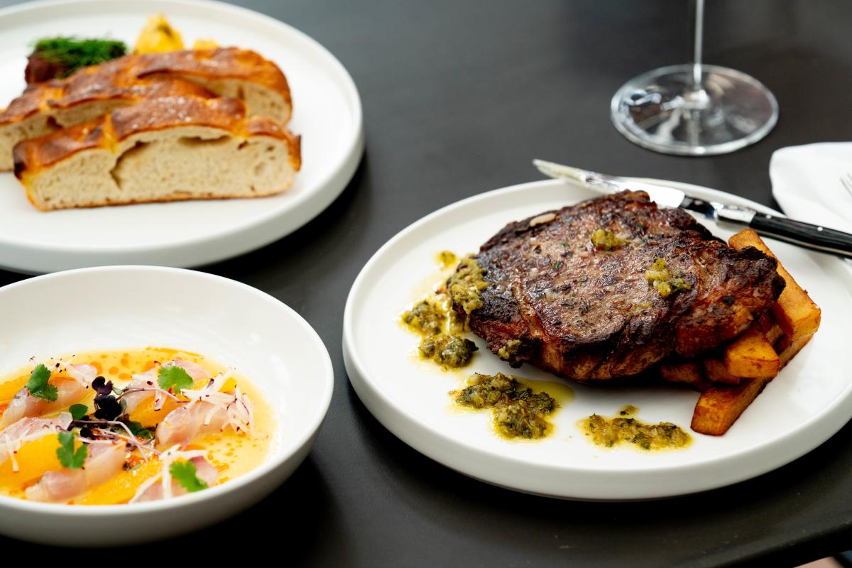 Plates of soup, steak with sides, and bread.