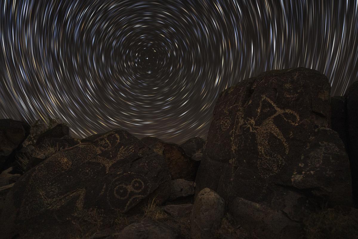 Petroglyphs on dark rocks under a swirling night sky create a mystical atmosphere.