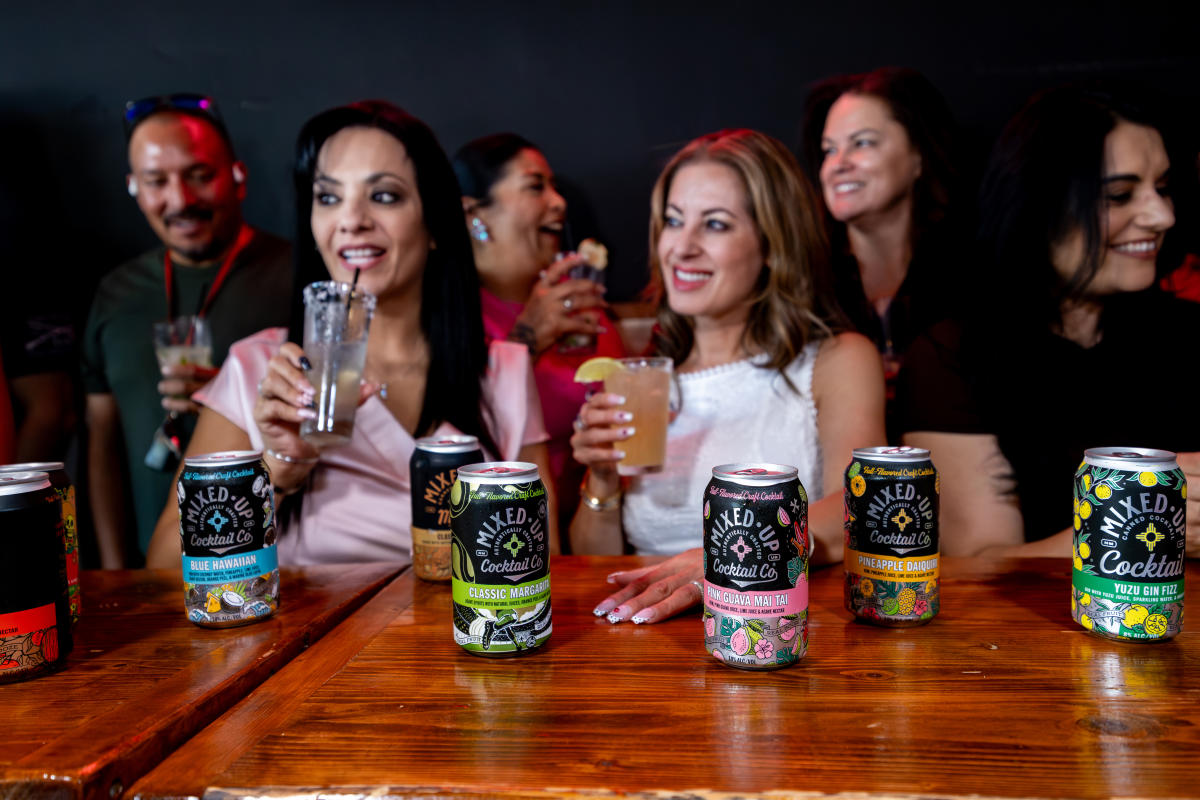 People at a bar drinking while Mixed-Up canned cocktails sit on the counter.