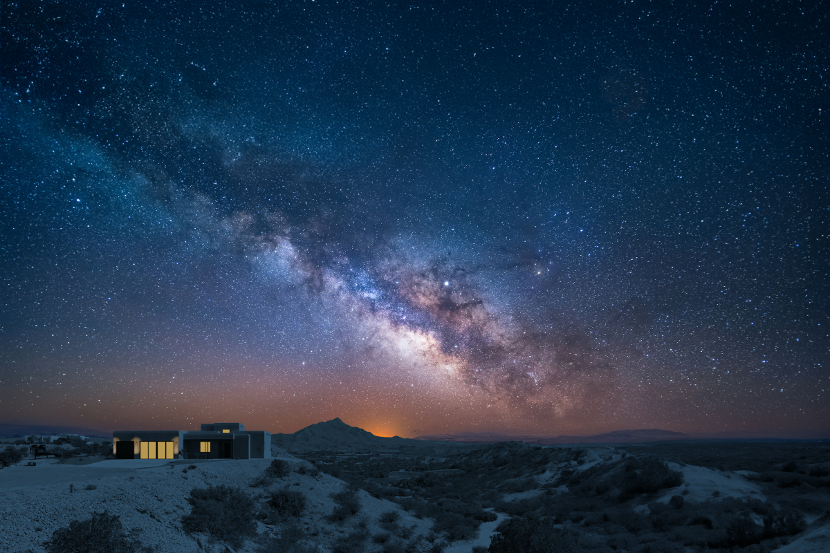 A desert house glows with warm light under a  star-filled night sky.