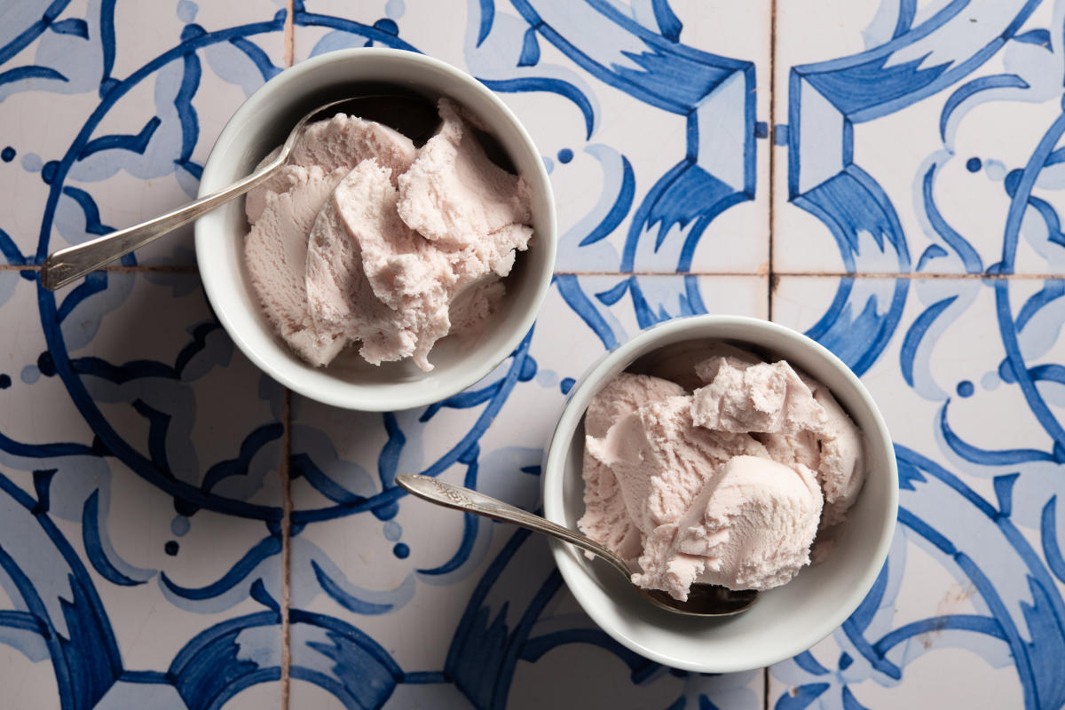 Two white bowls with light pink ice cream and spoons sit on a blue and white patterned tile surface.