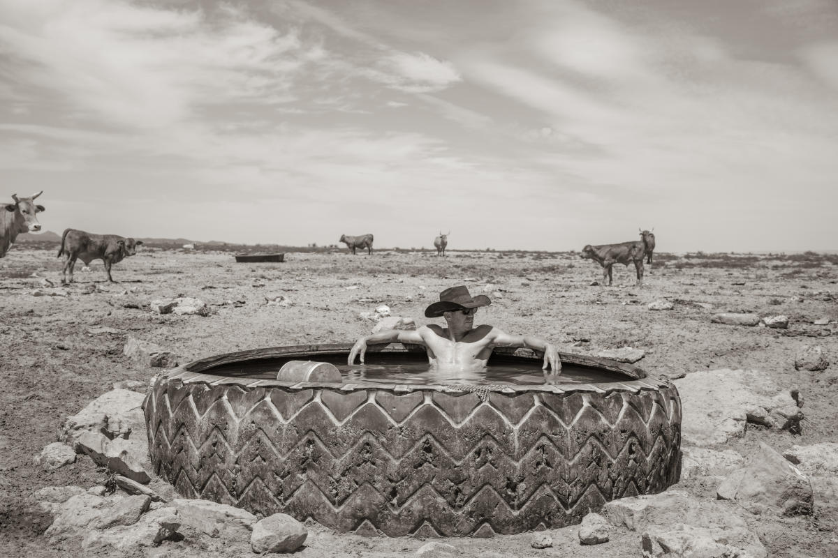 A ranch worker rests inside a large tire on an open New Mexico landscape.