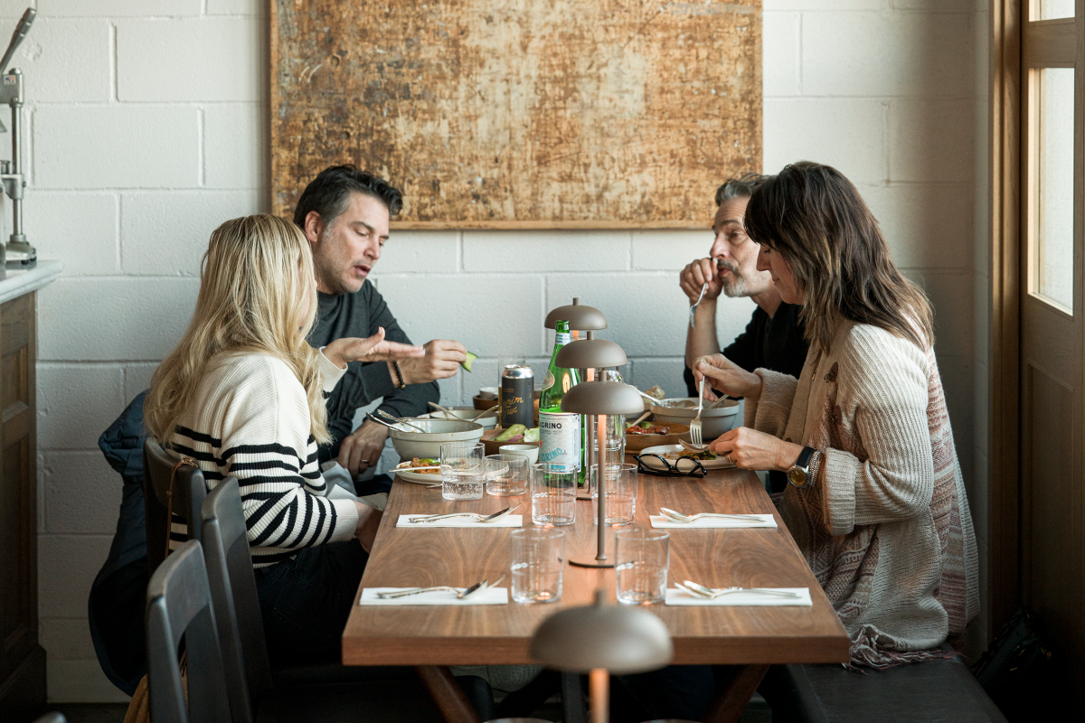 Four people sit around a wooden table in a cozy restaurant, engaged in conversation and eating.