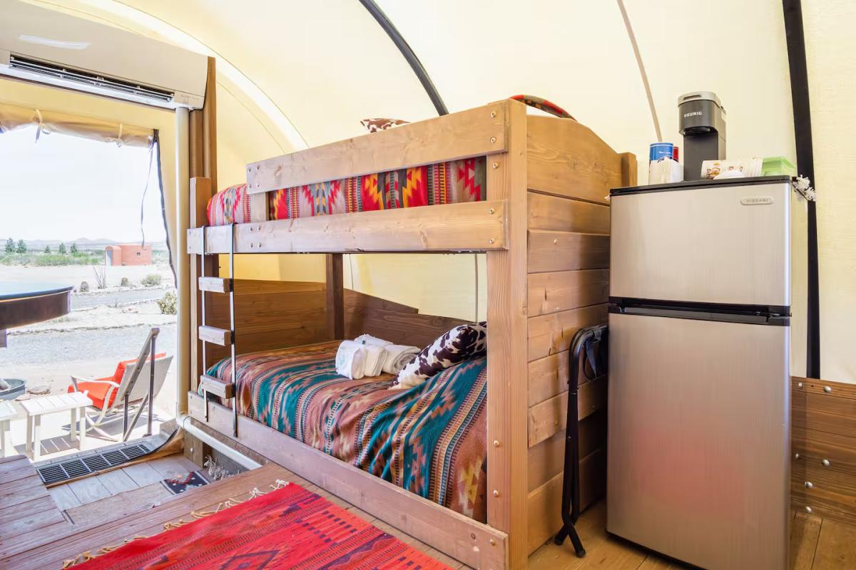 Interior of a glamping-style tent with wooden bunk beds covered in colorful blankets