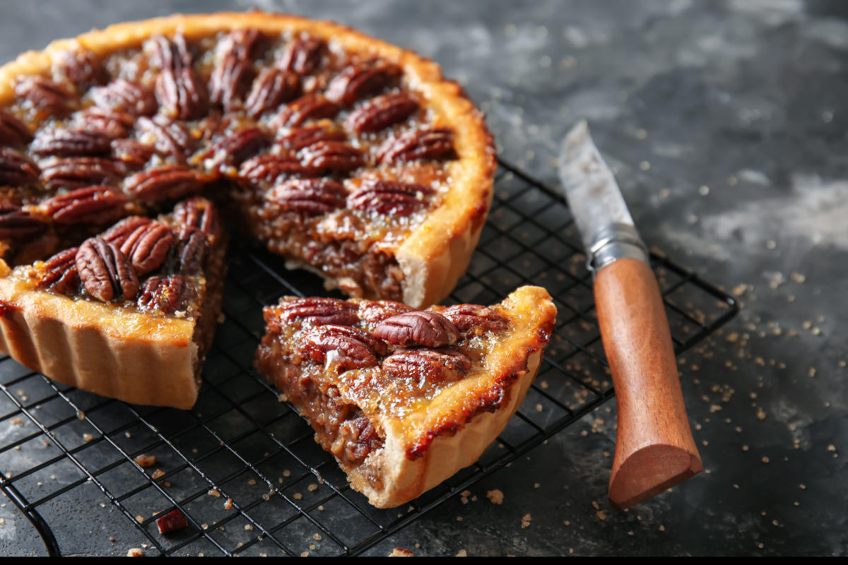 A pecan pie cooling on a rack has a slice cut out of it, waiting to be served.
