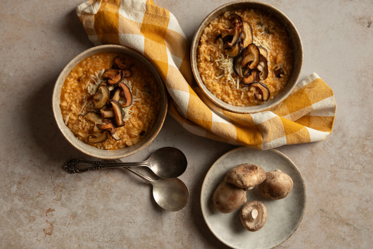Two bowls of creamy shiitake risotto topped with sautéed mushrooms and Chimayó chile, styled with a yellow checkered napkin.