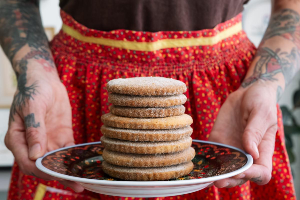 Person holding a plate of stacked cookies while wearing a red apron.