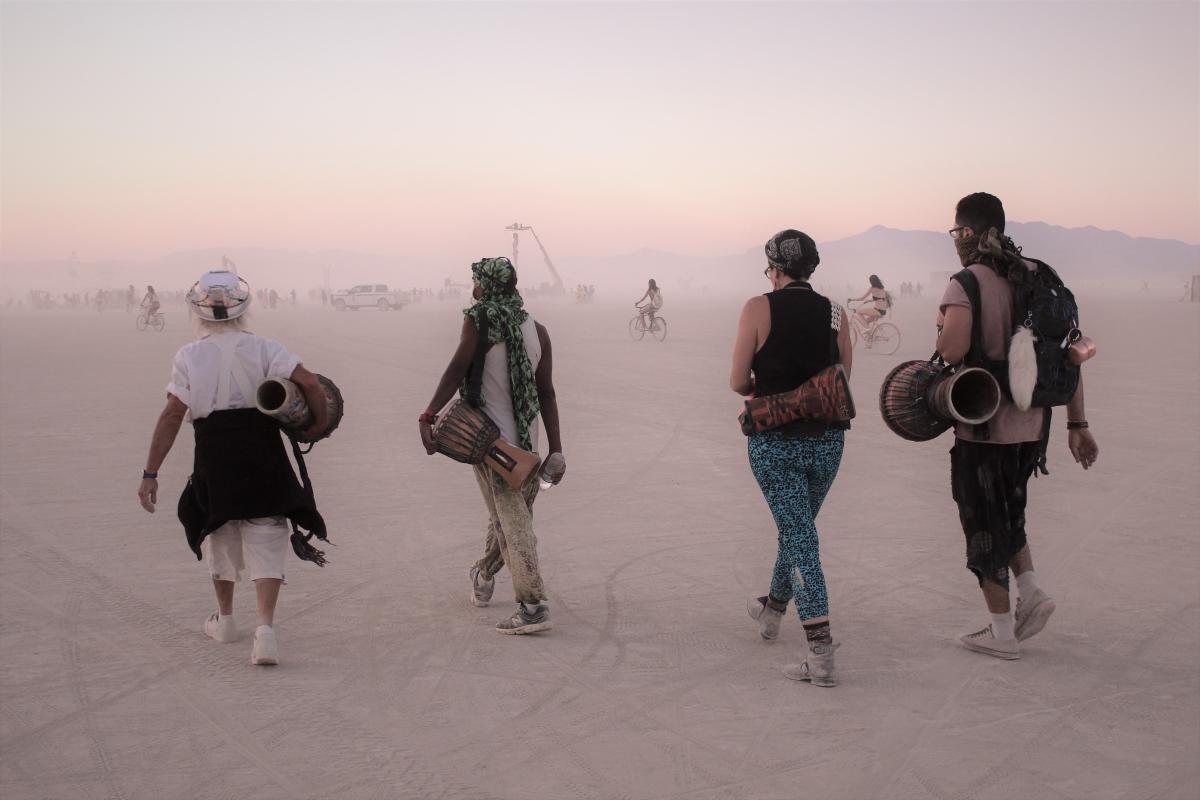 Four people walking across the dusty playa of Burning Man toward Black Rock City