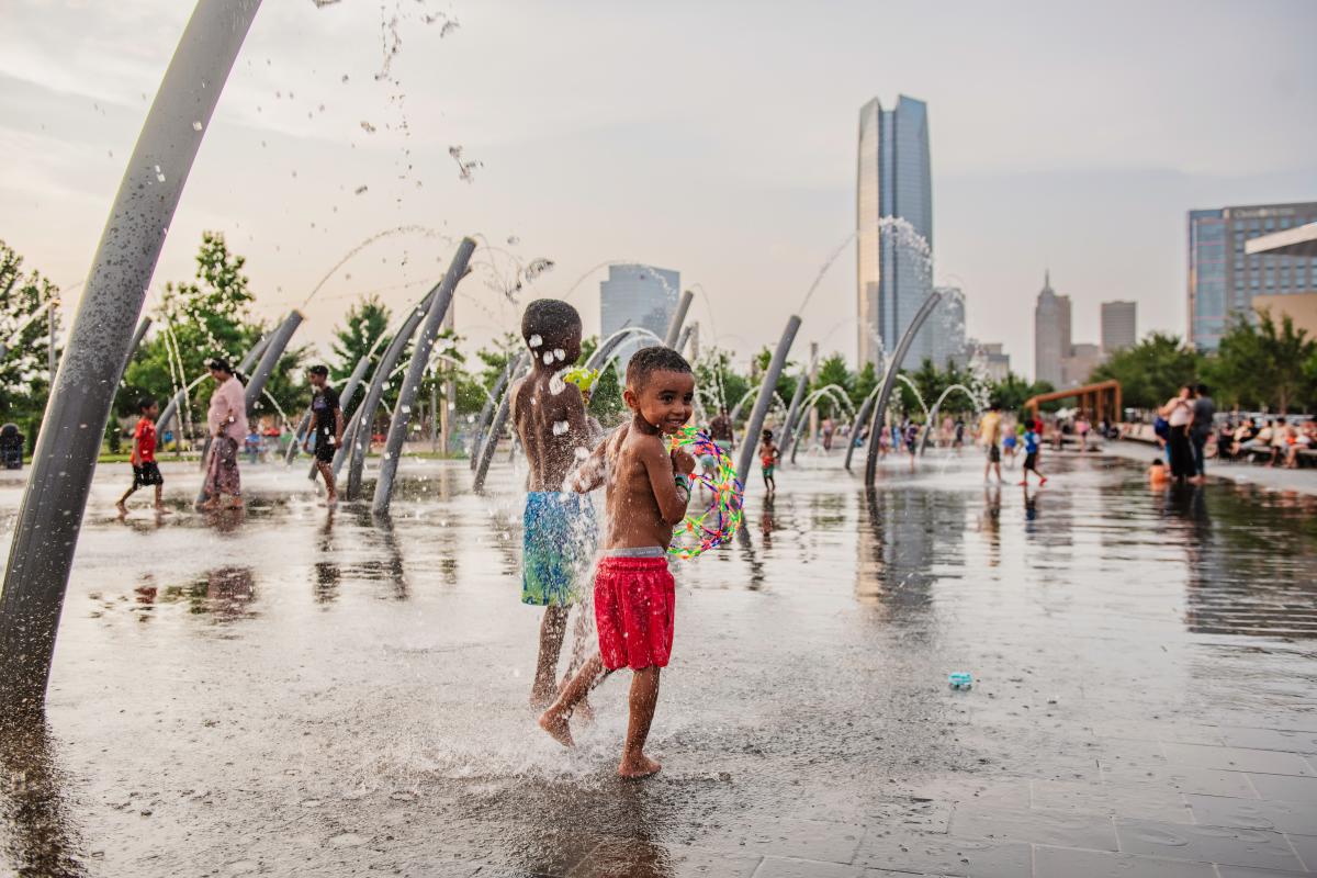 Children playing the splash pad at Scissortail Park. OKC skyline can be seen in the background.