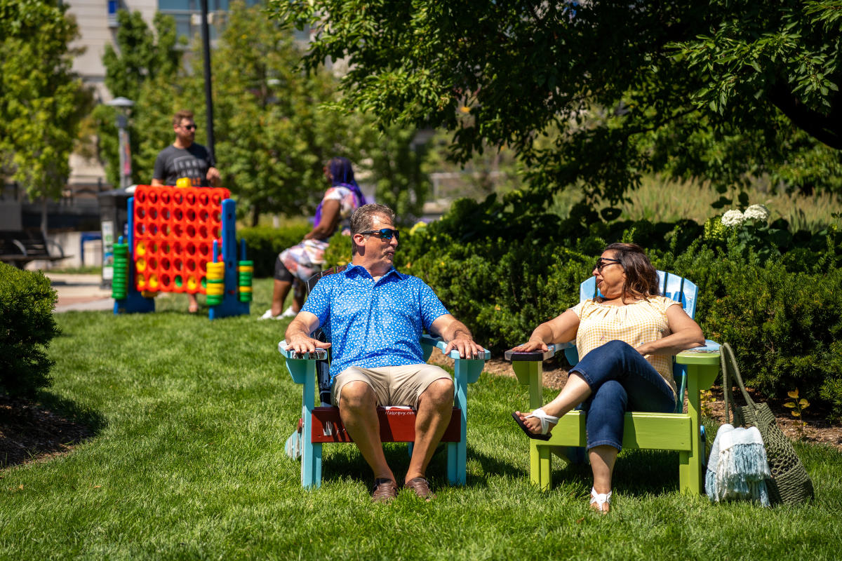 Two people sitting in hand-painted Adirondack chairs in the grass at Midtown Crossing.