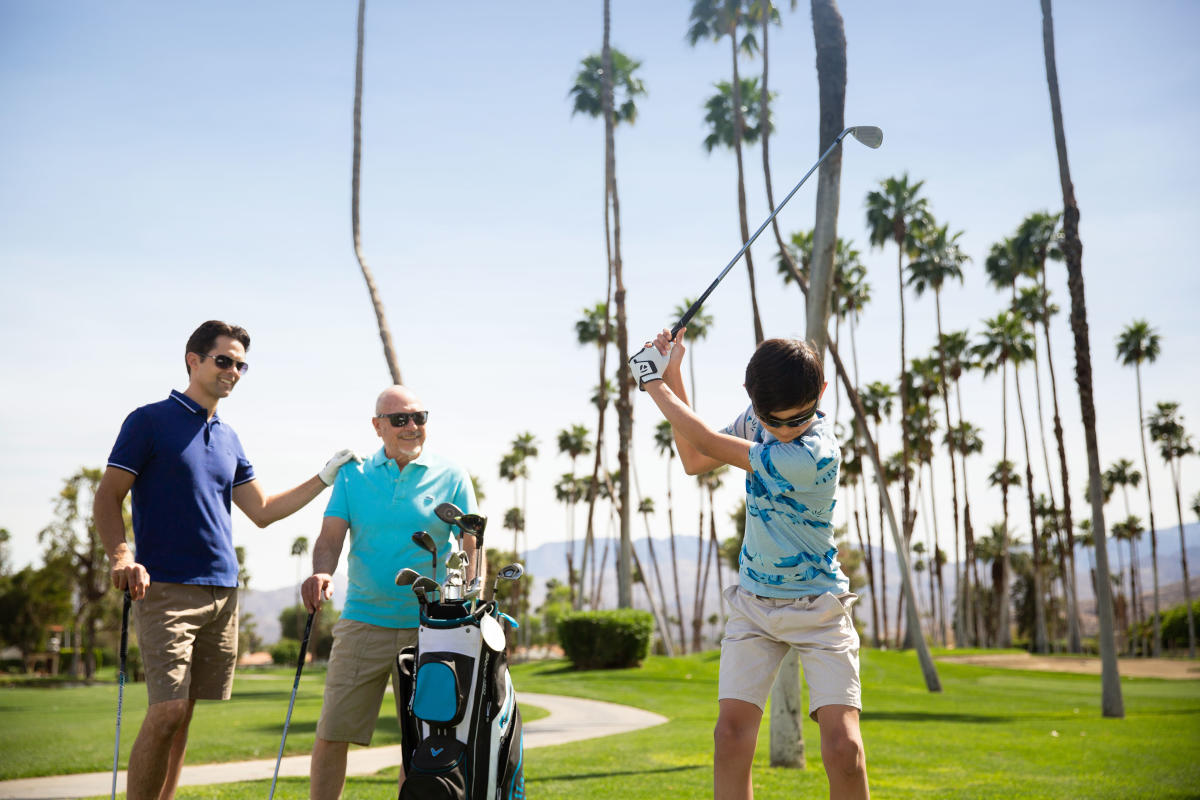 Two men and kid golfing with palm tree background