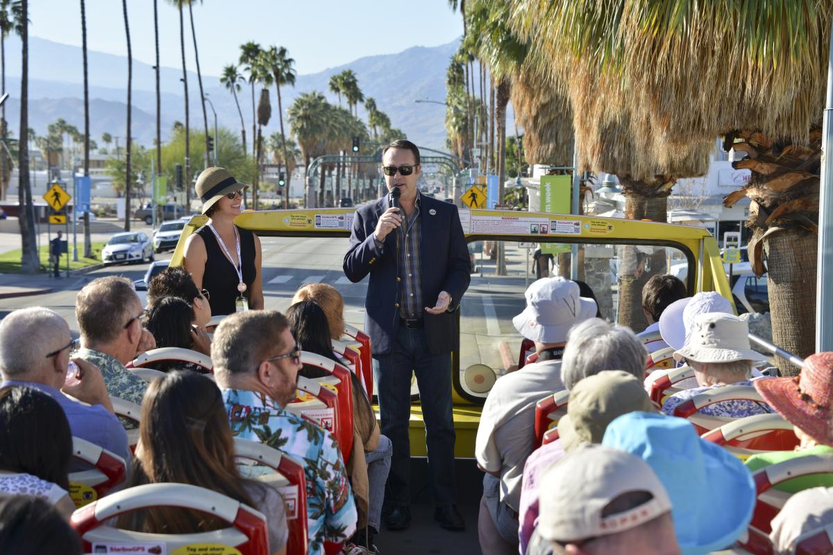 Modernism Week bus tour with tour guide and lots of people sitting in seats on the top deck of a double decker bus.