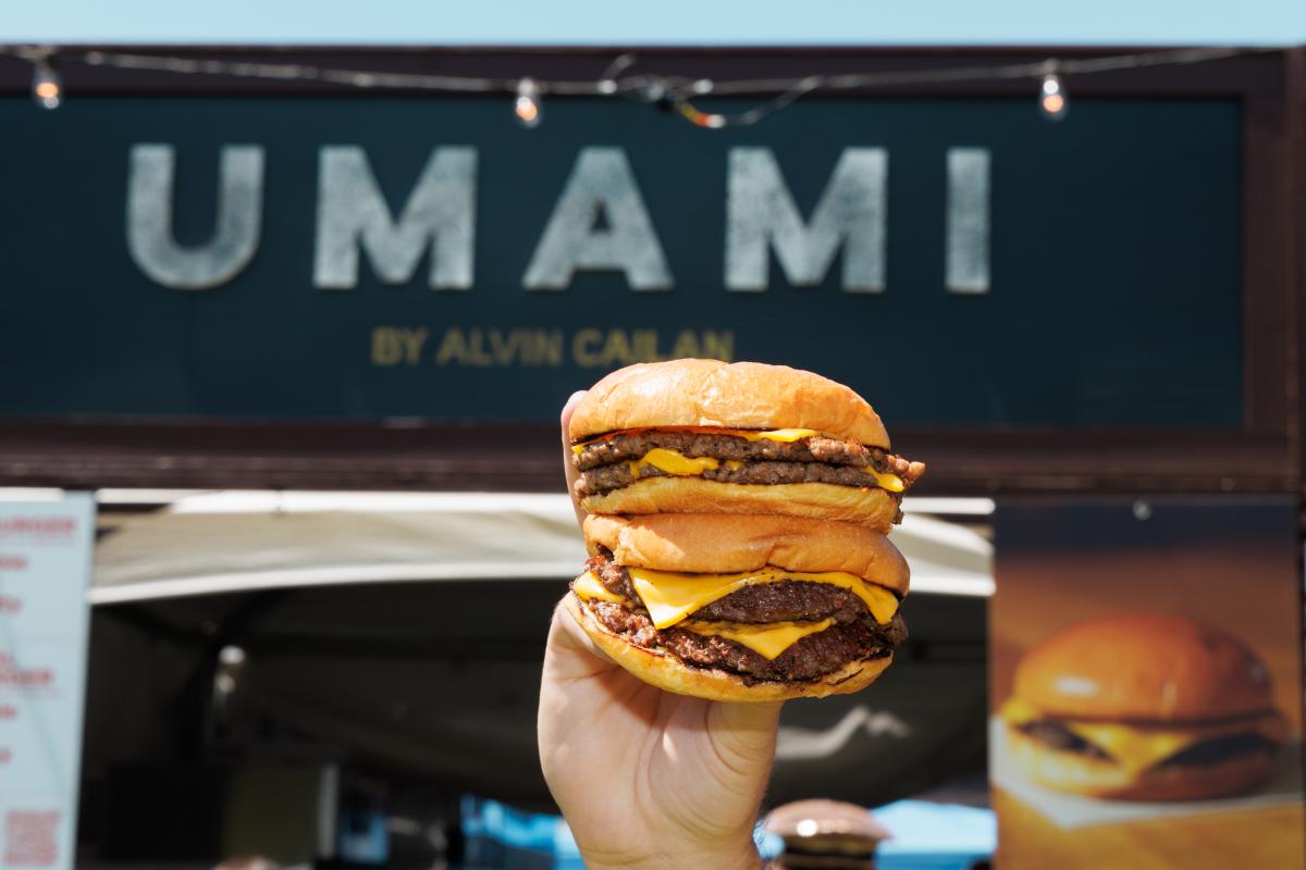 A huge, four-patty cheeseburger is held up in front of the Umami booth at Coachella Valley Music and Arts Festival.