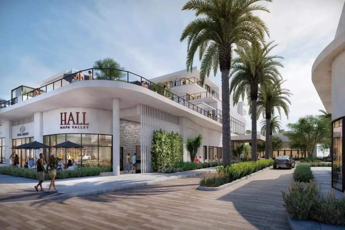 A digital rendering of a modern, two-story commercial building with "HALL Napa Valley" signage on the façade. People are walking and socializing on the ground and on the upper balcony. Palm trees line the walkway, and there's outdoor seating under umbrellas beside the building.