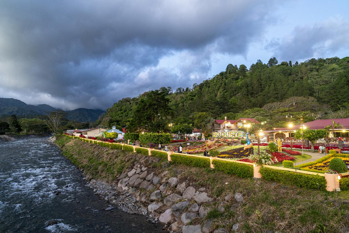 Vista panorámica de jardines en Boquete durante la feria de las flores, con montañas y río al fondo al atardecer.