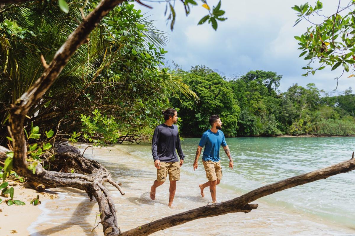 Two men walking along a jungle beach in Bocas del Toro, Panama