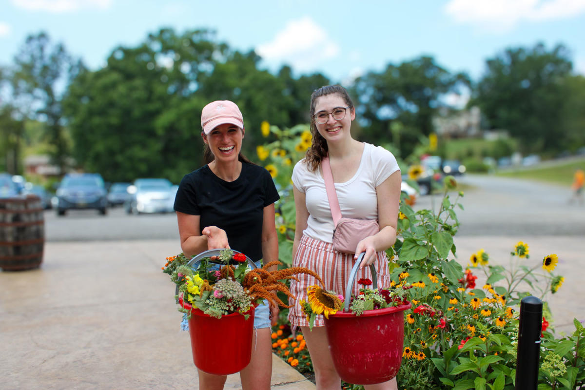 two women holding wildflowers in bucket