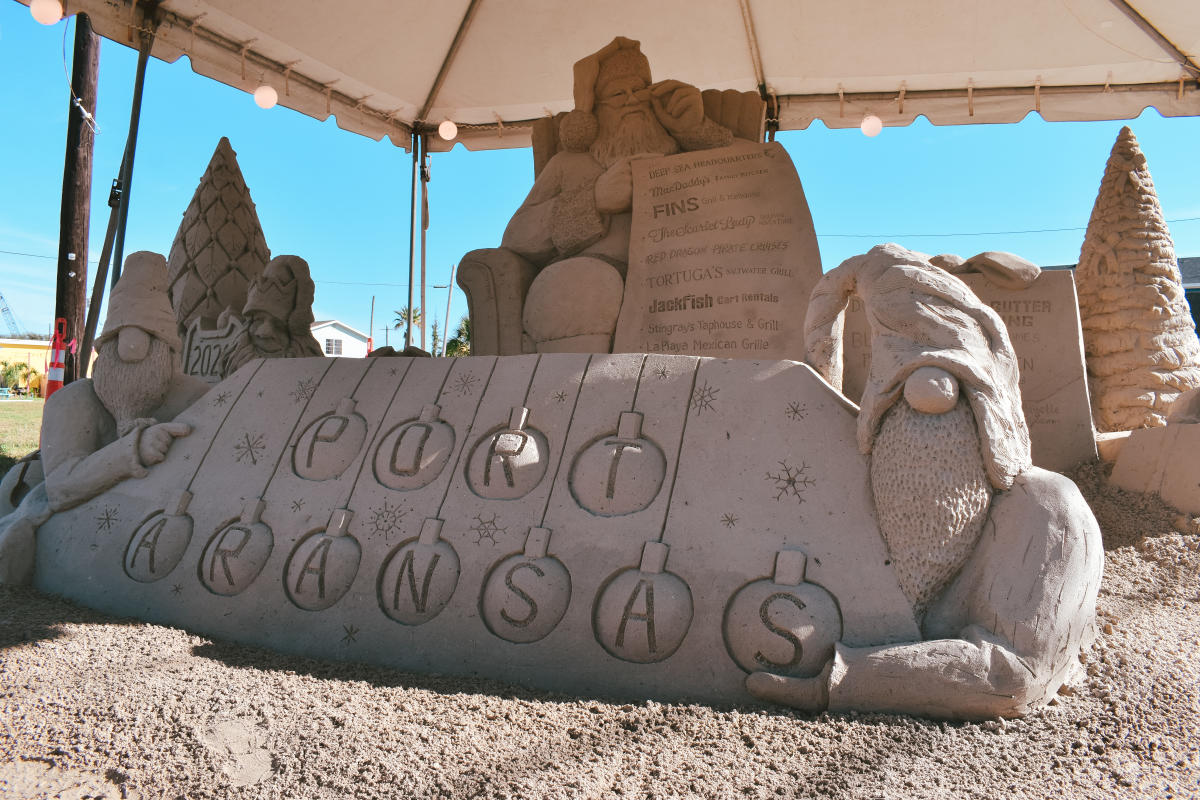 Sand sculpture of Santa's workshop. The focus is on a series of sand ornaments reading "Port Aransas."