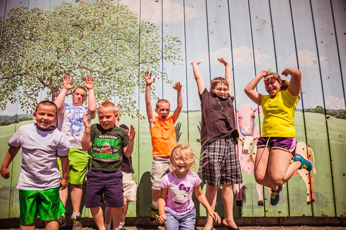 A group of children jumps excitedly in front of a nature mural