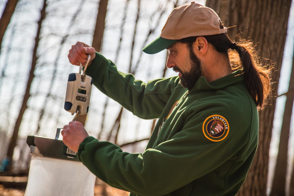 A man in a green sweatshirt with a volunteer patch on the sleeve reads a device
