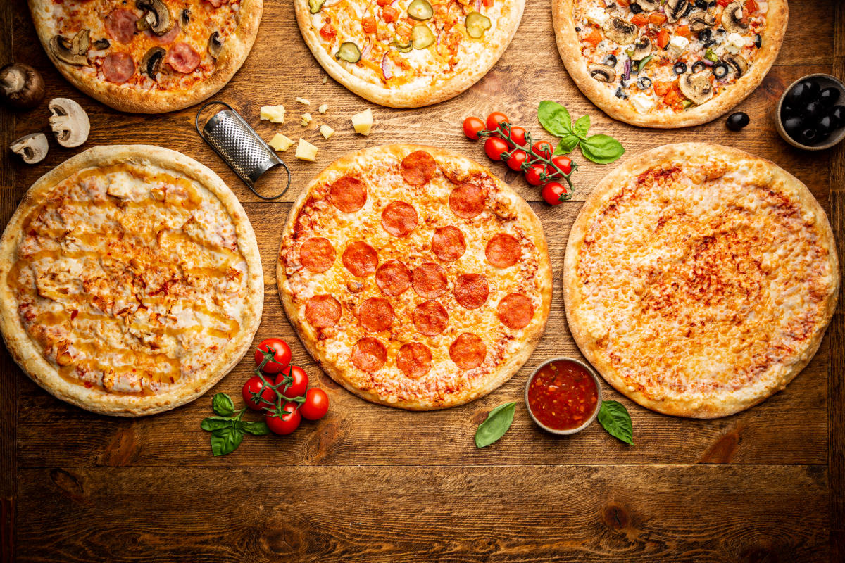 Six different types of pizza sit next to each other on a wooden surface