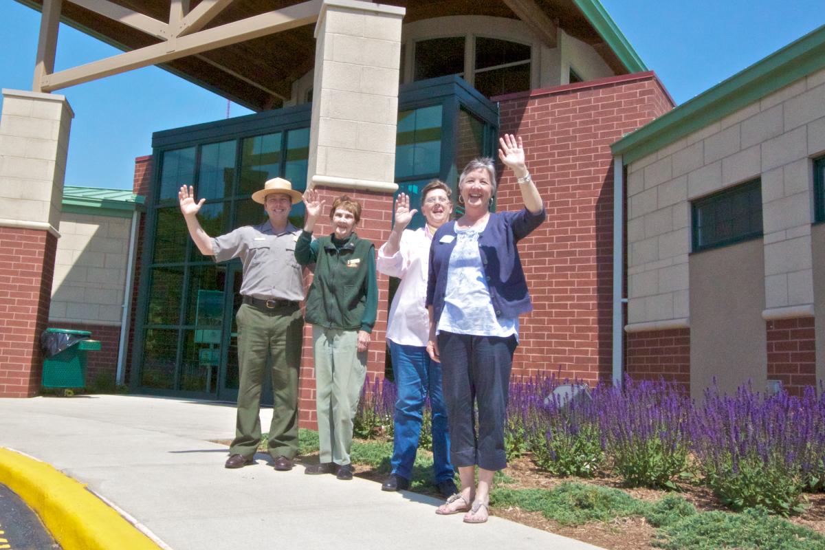 A park ranger in uniform stands with three women. All are waving.