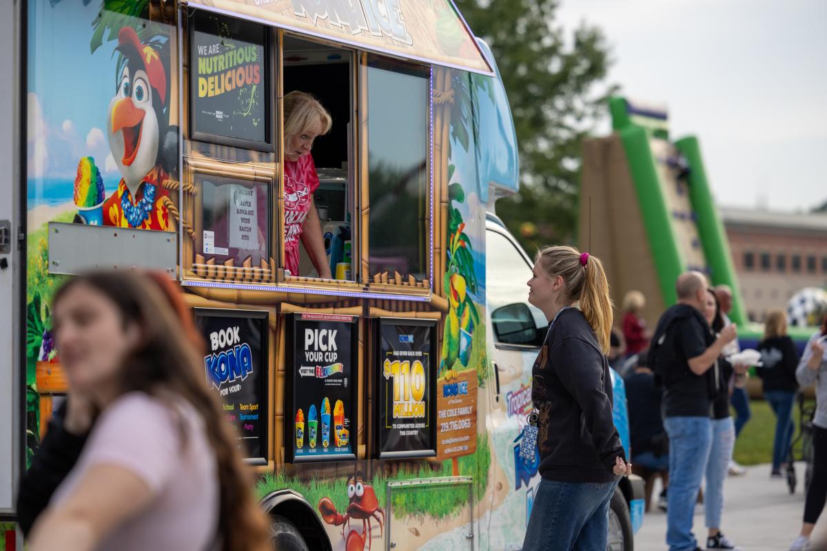 A woman looks out of a food truck window as she speaks to a customer.