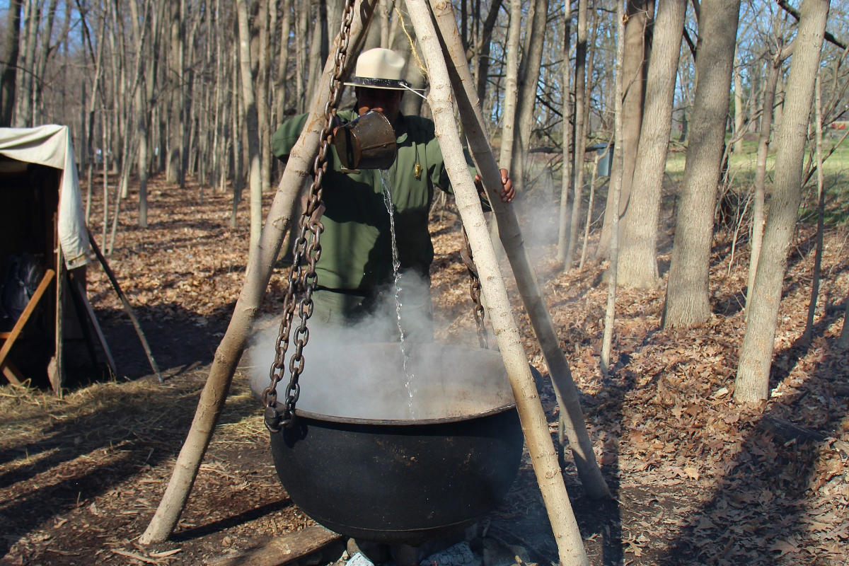 a park ranger stands behind a cauldron of boiling maple sugar