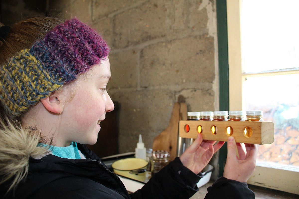 A girl with a winter headband on holds samples of maple syrup