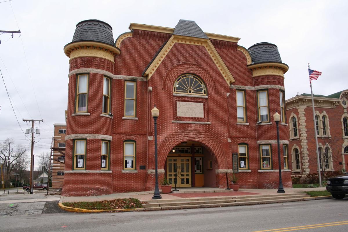 A historical red brick building with many windows and an arched doorway. The sky in the background is overcast.