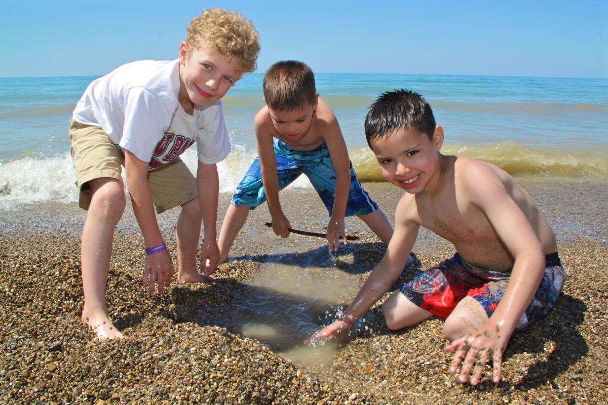 Three young boys play in the sand near the shoreline