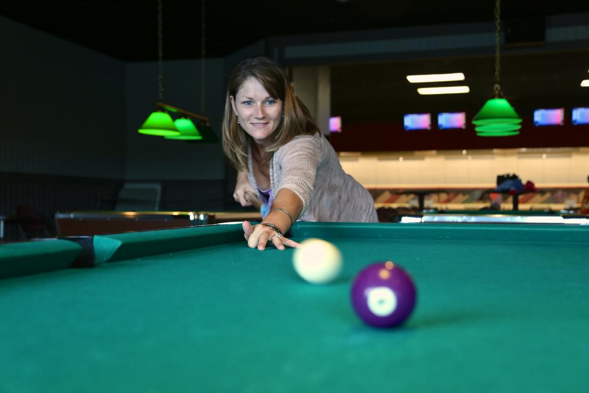 A woman leans over a billiards table shooting pool balls.