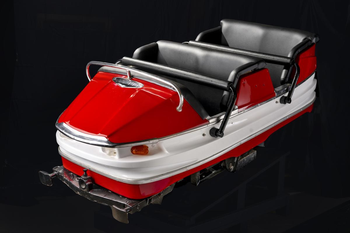 A red and white rollercoaster car with black leather seats and a black bar in front of the seats.