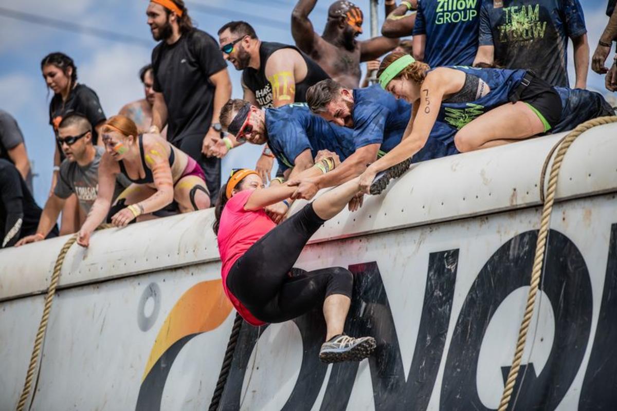 Adventure athletes pulling up female onto climbing wall at a tough mudder race.