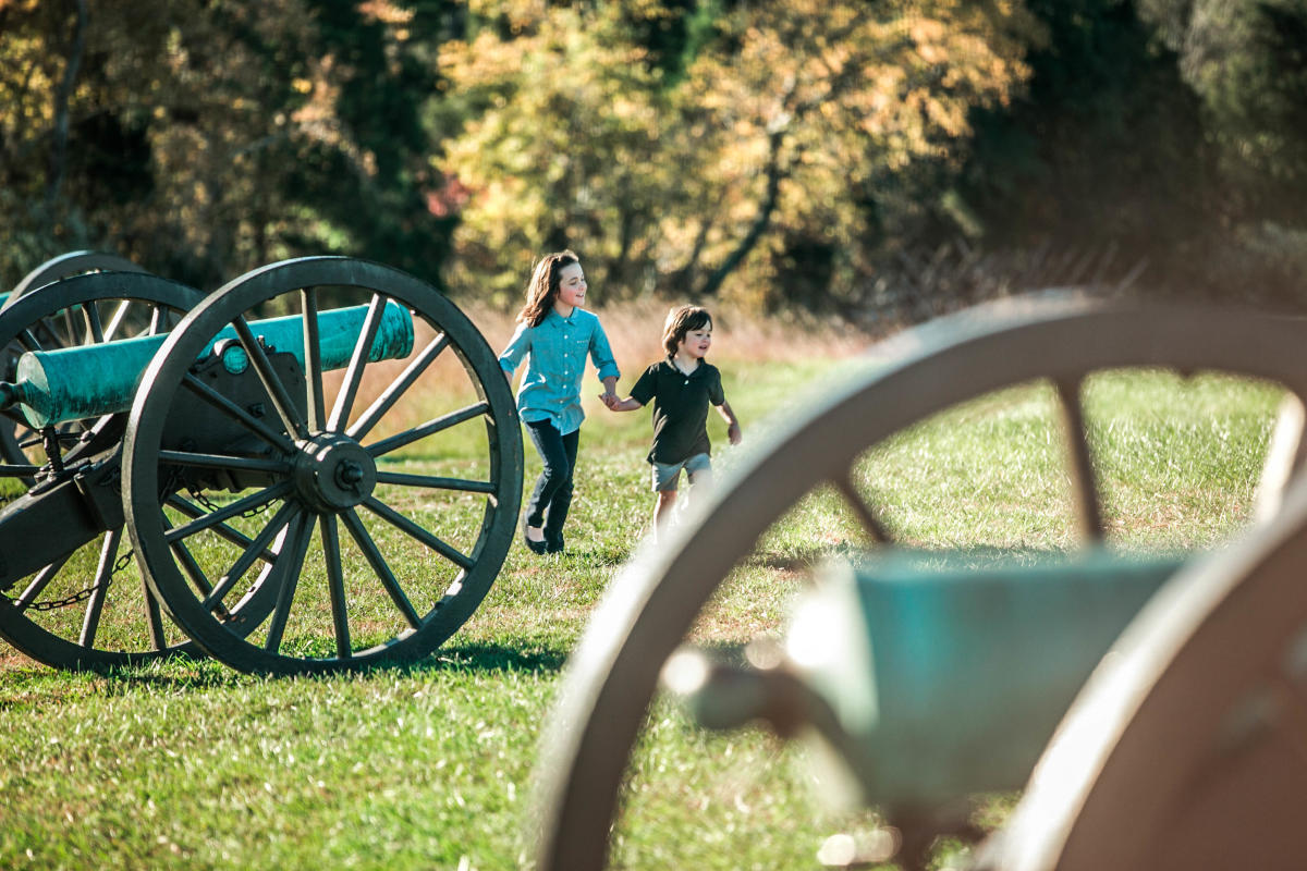 Two kids holding hands, walking on the field next to cannons