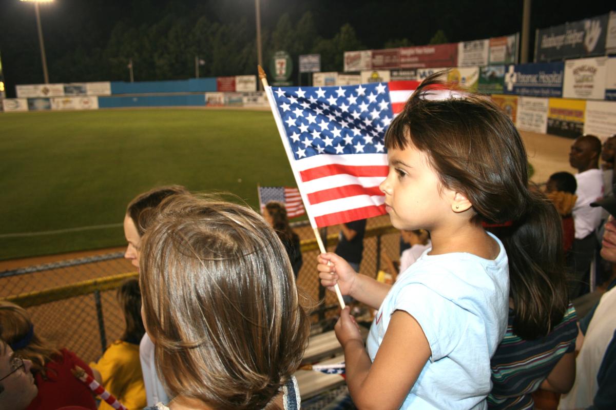 a girl holding a small flag at a baseball game