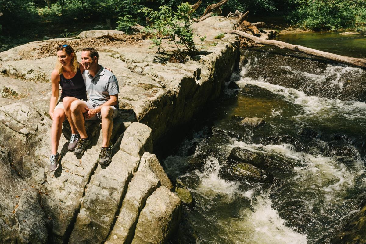 a couple sitting on the edge of a rock near water