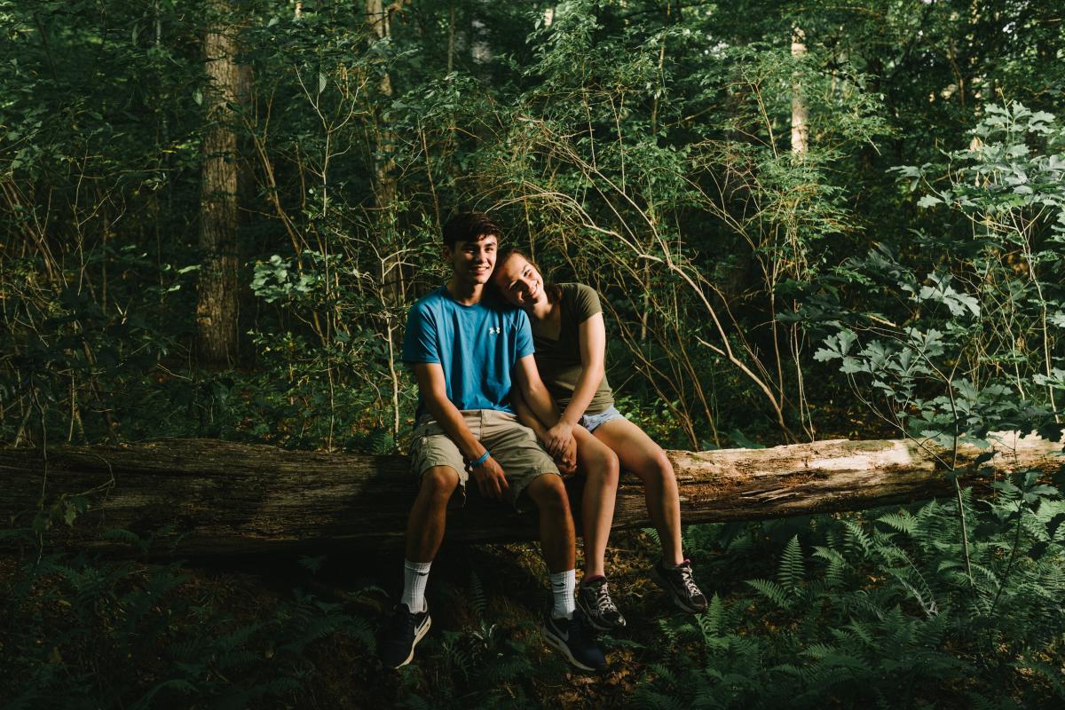 A young man and young woman sitting on a log in a forest