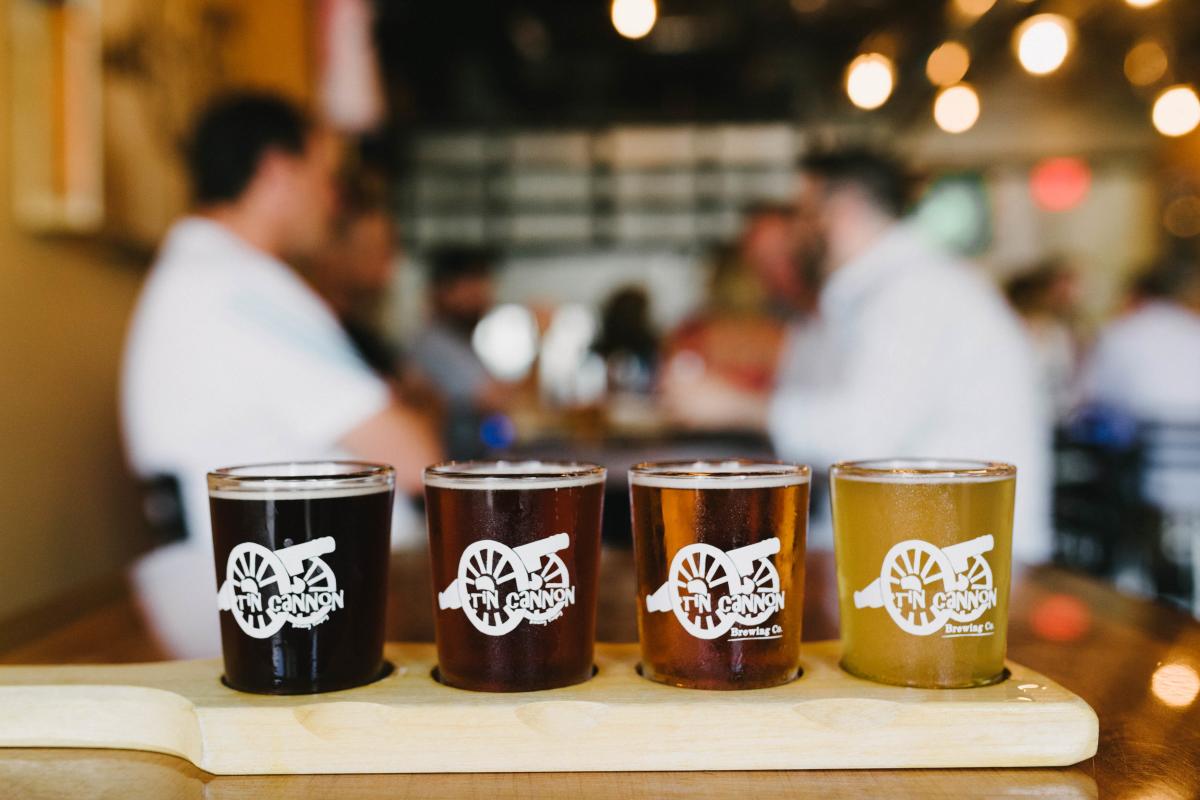 A flight of beers on a table with people sitting at a table in the background