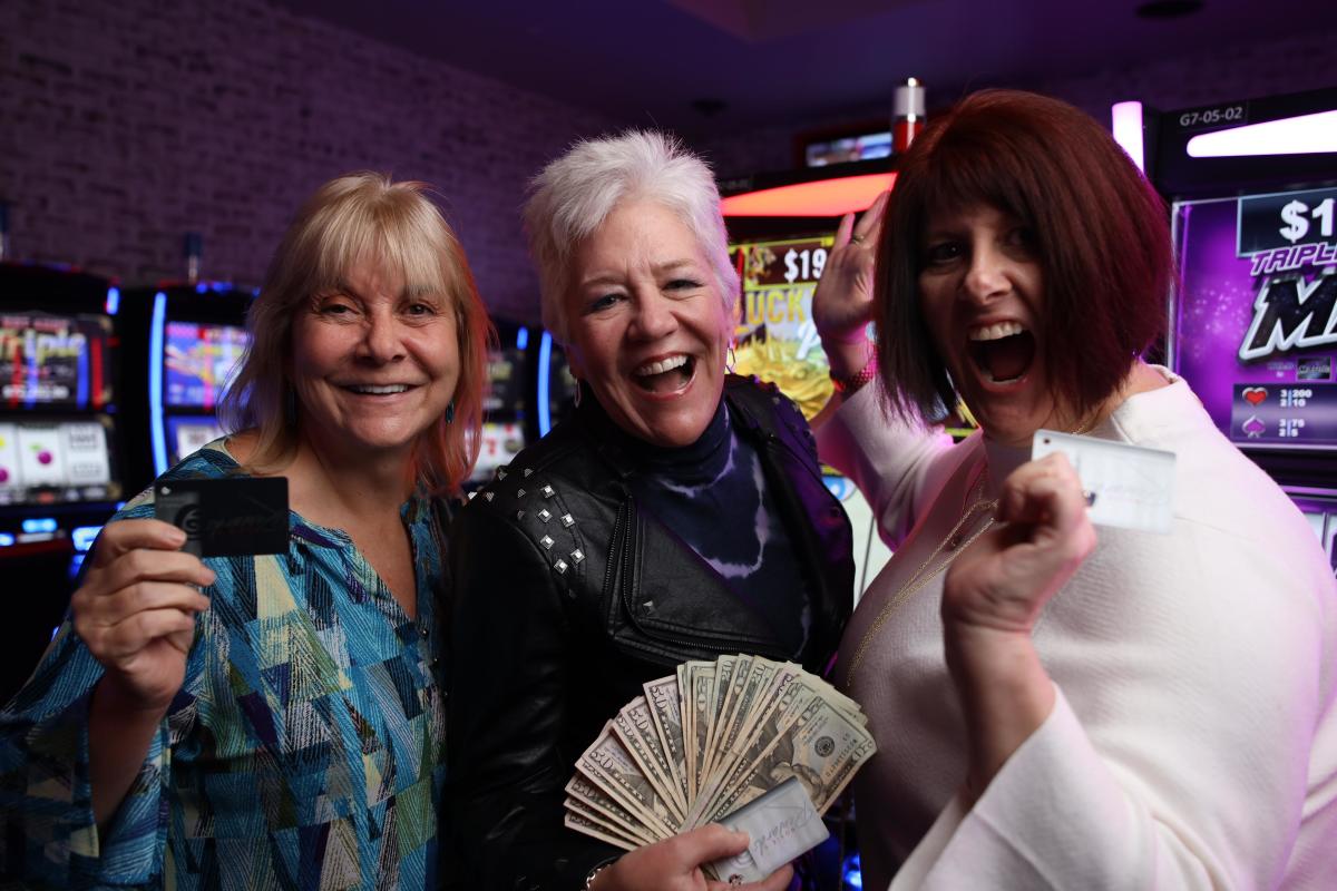 2 white women in front of gaming machines with their player card and money