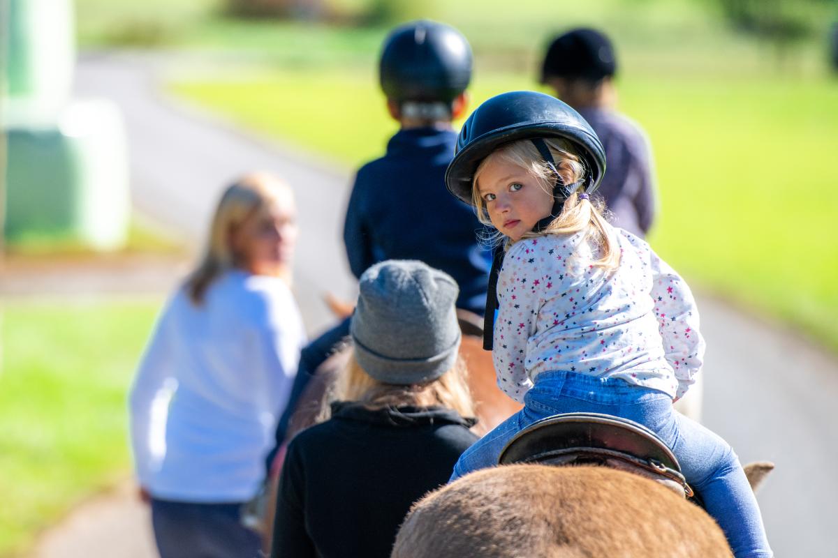 Young white girl looking over her shoulder on a horse being lead by an instructor