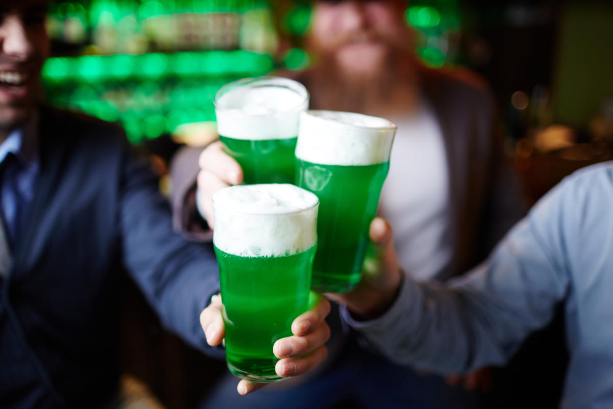 3 males holding up green beers