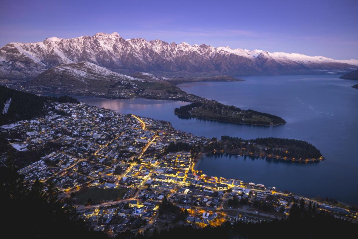 Aerial shot of Queenstown on a winters evening with town street lights glowing and snow capped mountains in the background