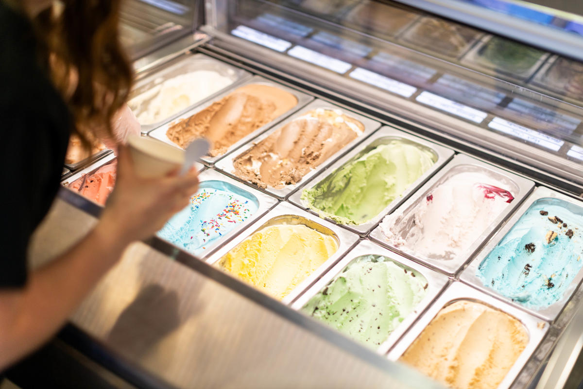 A person selects from a colorful array of ice cream flavors in a display case. Options include chocolate, mint and strawberry, evoking a joyous, indulgent mood.