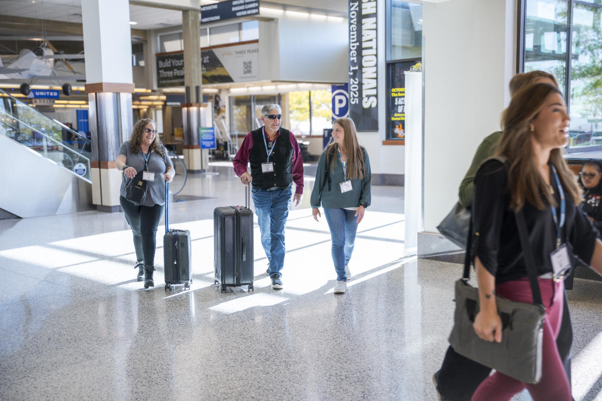 Conference attendees with luggage walk through a bright airport terminal.